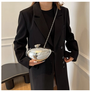 Detail view of mirror silver pebble handbag with metal chain against black suit