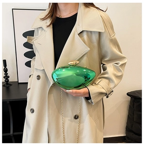 Detail of emerald green metallic evening bag with gold chain strap held by a model
