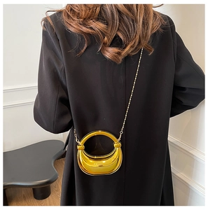 Detail der gold-metallischen Sichel-Handtasche mit rundem Griff und langer Kette
