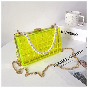 Détail du sac en acrylique jaune néon avec poignée en perles et chaîne dorée sur surface chic