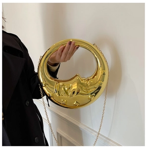 Close-up of golden moon-shaped evening bag with a metallic mirror finish and chain
