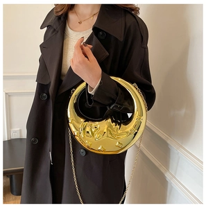 Detail of golden moon-shaped clutch with celestial relief and fine chain strap
