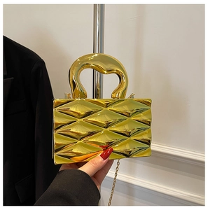 Detail of a gold metallic box bag featuring a geometric 3D pattern and an organic handle