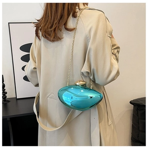 Metallic blue evening clutch bag with gold chain strap shown on model over a beige trench coat