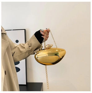 Close-up of a pebble-shaped gold evening clutch with a polished mirror finish and chain