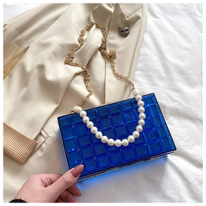 Pochette bleue en acrylique avec anse perle et chaîne dorée sur un blazer beige