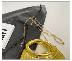 Detailed close-up of metallic pleated gold handbag with delicate chain strap on blazer