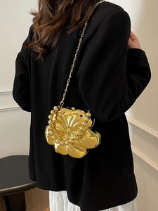 Detailed view of a gold flower-shaped clutch bag with elegant metal chain on model