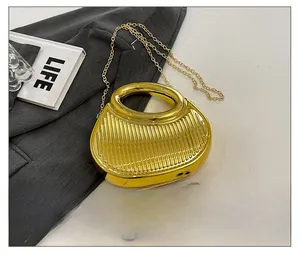 Detail of gold semicircular clutch with vertical stripes and metal chain next to a phone