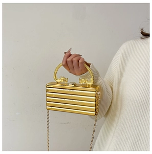 Close-up of golden acrylic box bag featuring ornate dragon handles and ribbed texture