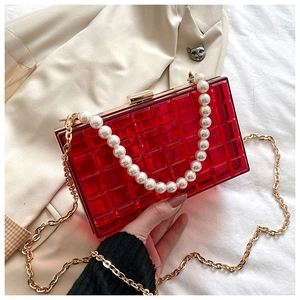 Détail d'une pochette en acrylique rouge avec chaîne de perles et bandoulière dorée