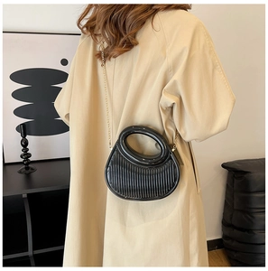 Detail of black pleated crossbody bag with round hollow handle and gold chain strap