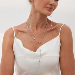 Detail view of a long silver bead Y-chain necklace and matching drop earrings on a model