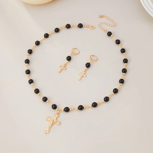 Détail du collier avec pendentif croix dorée et boucles d'oreilles perlées sur beige