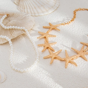 Detailed view of gold starfish pendant and white pearl beads on white sand background