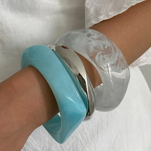 Gros plan de bracelets en résine superposés à texture marbrée et jonc en métal poli