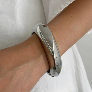 Bracelet jonc large en résine argentée polie porté au poignet avec design arrondi