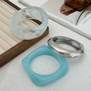Détail de l'ensemble de joncs en résine et argent sur un plateau de bijoux beige