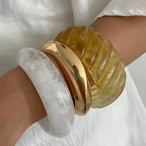 Close-up of stacked resin marble, gold metal, and amber twist bangles on a wrist