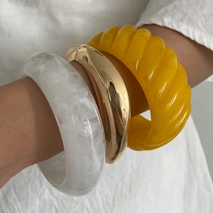 Detail of resin marble and gold metal bangles stacked over white linen fabric