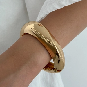 Close-up of a wide polished gold chunky bangle featuring a high-gloss mirror finish