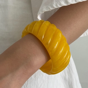 Detail of a wide yellow resin bangle featuring a modern spiral ribbed texture for women