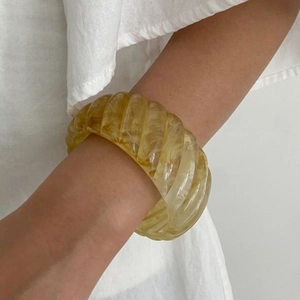 Detail of an amber resin wide bangle featuring a retro spiral texture and translucent finish