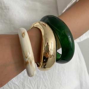 Close-up of stacked chunky resin bracelets in cream marble, gold and dark green tones