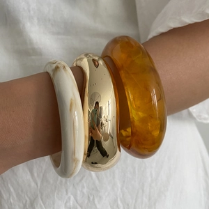 Close-up of three stacked resin and gold-polished metal bangles on a woman's wrist