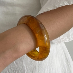 Detailed view of a wide amber resin bangle with natural swirling texture on wrist