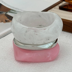 Detail of chunky resin bangles with marble texture and silver metal rings on a wooden tray