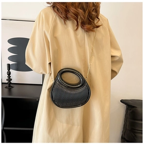 Detail of black semi-circular pleated handbag with gold chain on model's beige trench coat