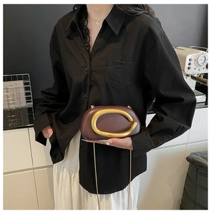 Detail der weinroten Clutch mit goldenem C-Logo und eleganter Gliederkette für Damen