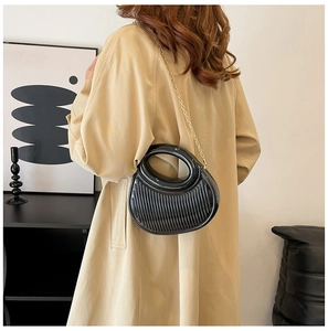 Lifestyle shot of black pleated crescent bag with gold chain on model in trench coat