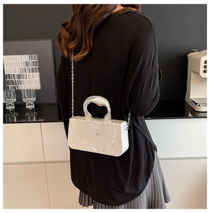 Détail de la pochette en acrylique marbre blanc avec poignée argentée et chaîne sur modèle