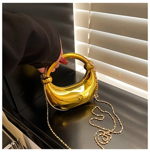 Detail der glänzenden goldenen Sicheltasche mit rundem Metallgriff und Perlenkette