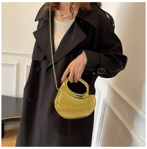 Close-up of semi-circular gold metal handbag with textured finish on a black coat