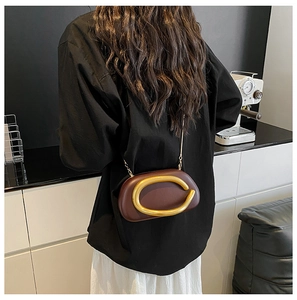 Detail einer dunkelbraunen Ledertasche mit großem Goldring und eleganter Goldkette