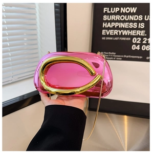 Detail of glossy pink metal clutch bag featuring bold gold C-handle and fine chain strap
