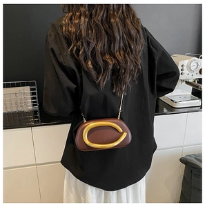 Detail einer dunkelbraunen Abendclutch mit großem mattgoldenen ovalen Beschlag und Kette