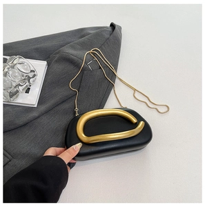 Detail der schwarzen Leder-Clutch mit goldenem Metallgriff und eleganter Schlangenkette
