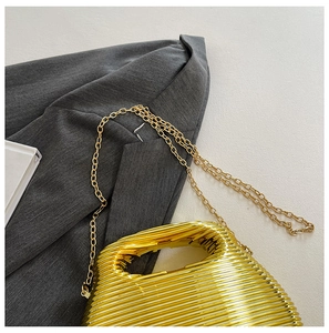 Close-up of golden metallic ribbed evening bag with elegant chain strap on grey blazer