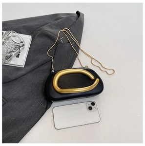 Detailansicht der schwarzen Clutch mit goldfarbenem Ringgriff und Kette auf einem Blazer
