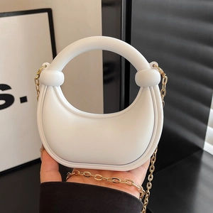 White mini handbag with knot handle and gold chain strap shown in a fashion-style hand-held pose