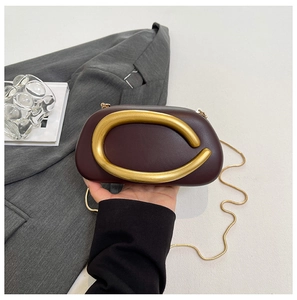 Detail der burgunderroten Leder-Clutch mit skulpturalem Goldgriff und Kettenriemen