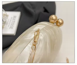 Detail of cream acrylic clutch featuring shell texture and gold spherical clasp