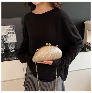Detail of golden marble textured shell evening clutch bag with pearl clasp and chain