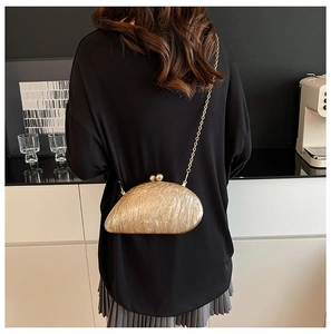 Detail of champagne shell evening bag with golden chain strap on a modern background