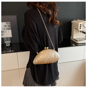 Detail of shell-shaped marble acrylic clutch bag with golden chain and sphere clasp