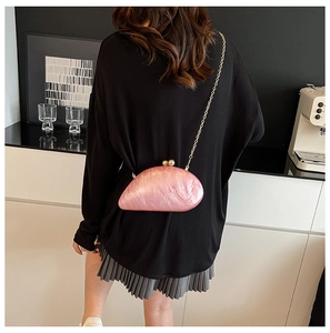 Pink marble acrylic shell clutch with gold chain shown on a model in a modern room